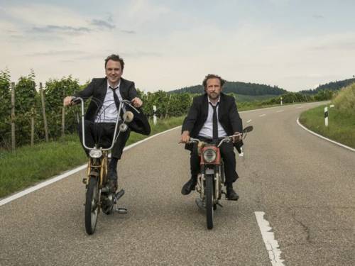 Bjarne Mädel und Lars Eidinger fahren auf Mofas einen Feldweg entlang